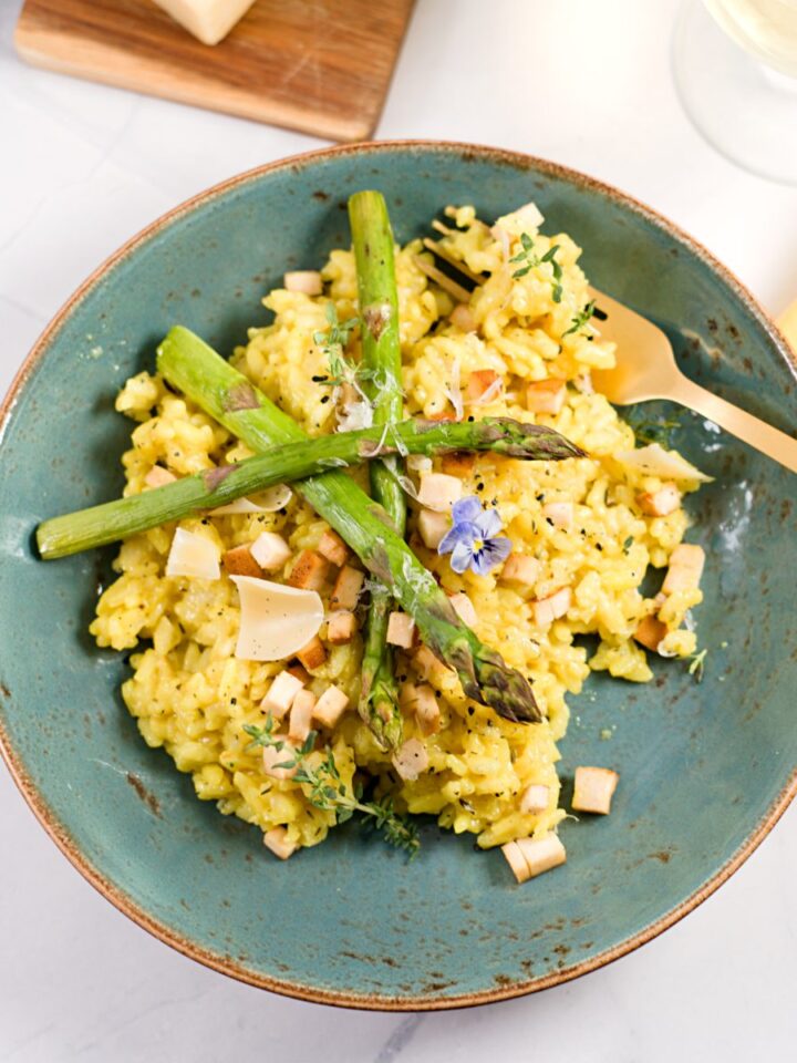 lemon risotto on plate with asparagus, tofu, blue flower decoration.