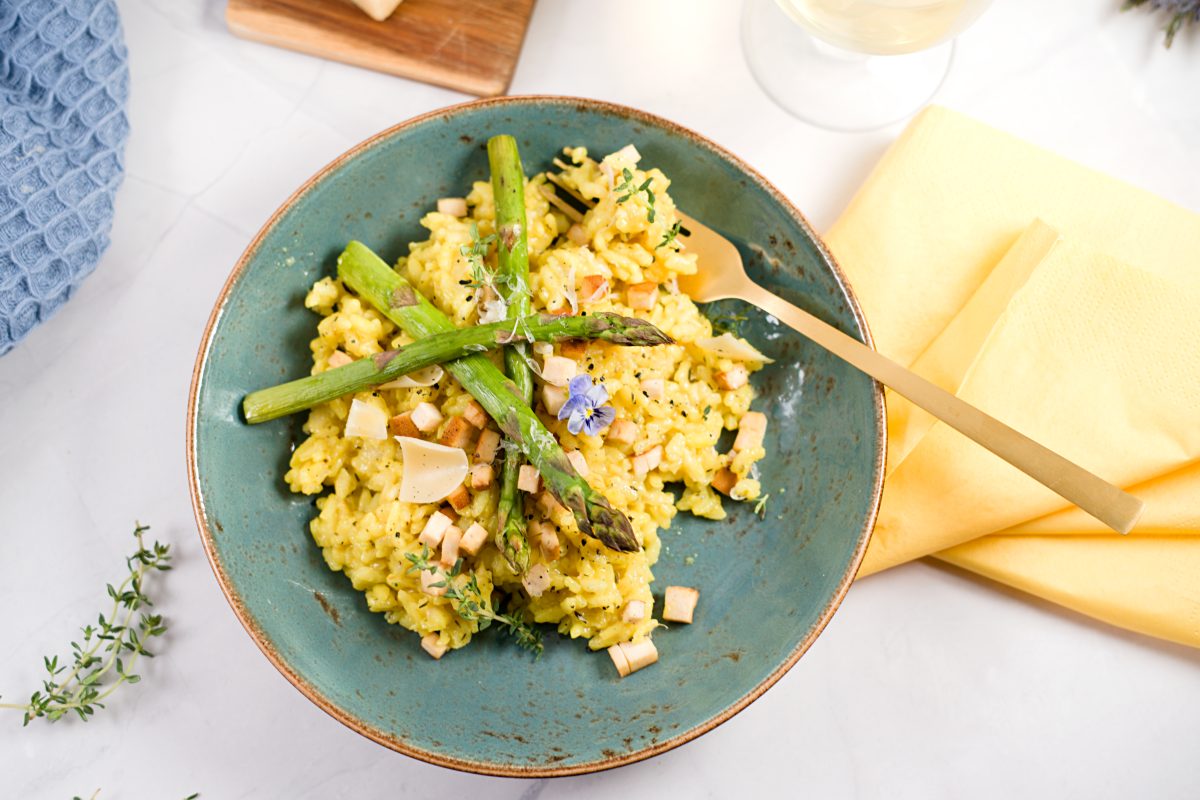 yellow risotto on blue plate with 3 asparagus and small tofy cubes. 